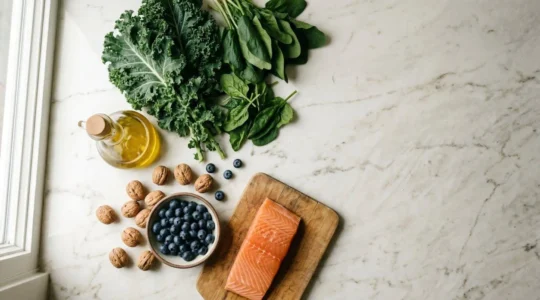 Overhead view of vibrant Mediterranean-style meal preparation with fresh leafy greens, olive oil, and colorful vegetables arranged naturally on a kitchen counter